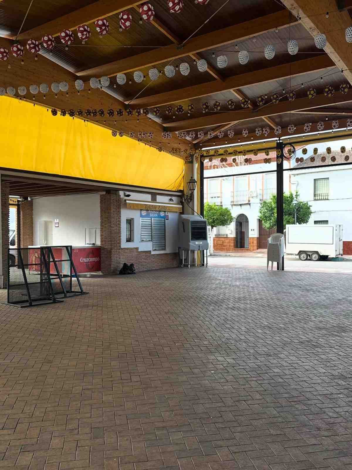 Patio cubierto pavimentado con ladrillos, vigas de madera, pared amarilla y mesas al aire libre bajo una estructura techada.