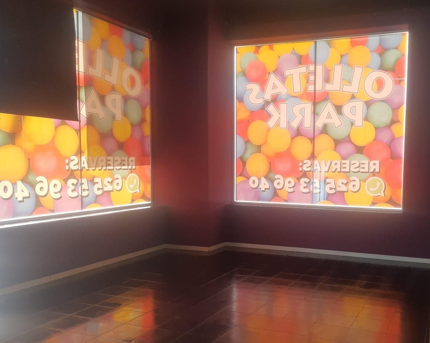 Sala de galería vacía con dos escaparates llenos de globos de colores y suelos oscuros pulidos.