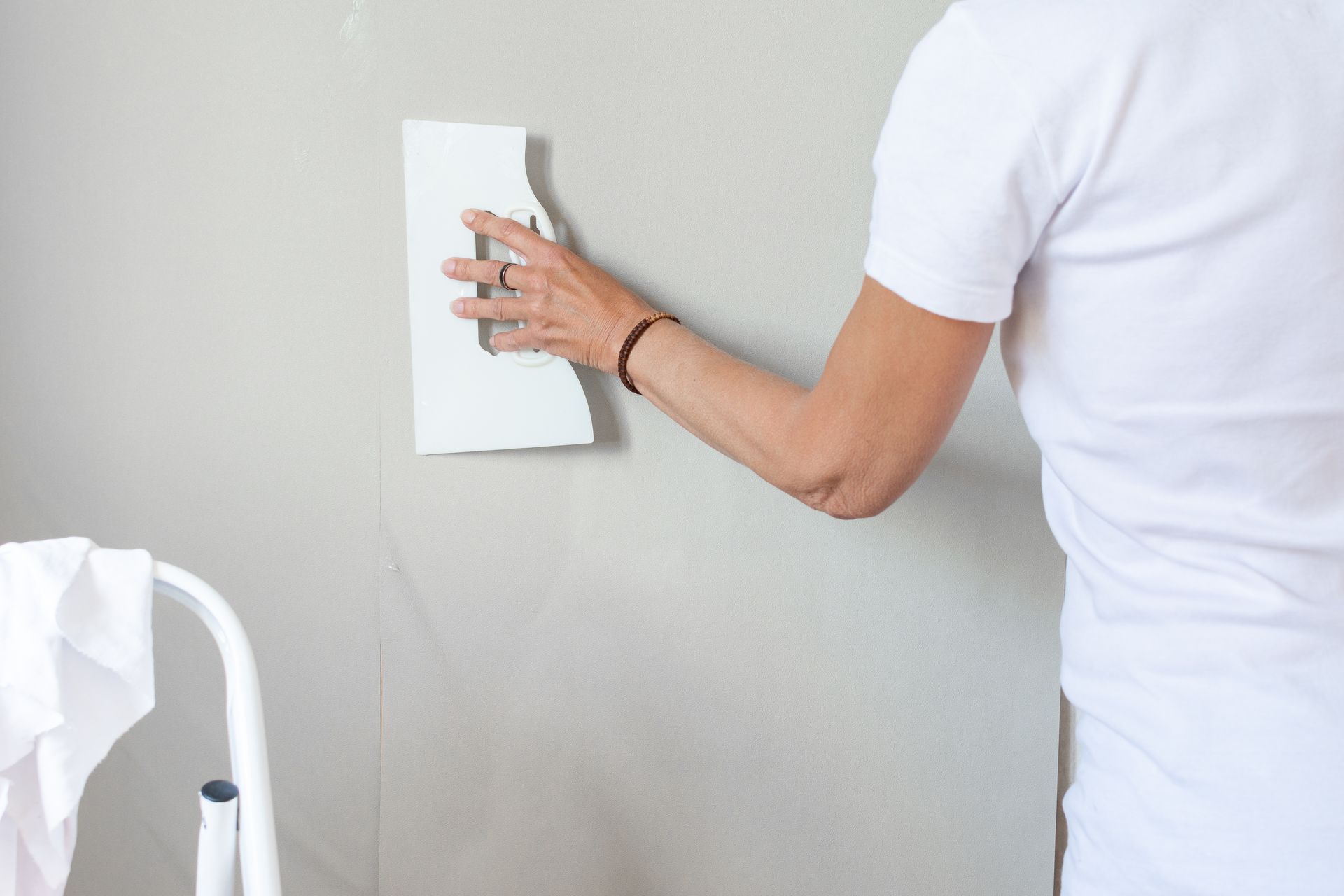 Main utilisant un rouleau à peinture, peignant en bleu sur un mur blanc.