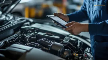 Mecánico examinando el motor de un coche con una tableta en un garaje.