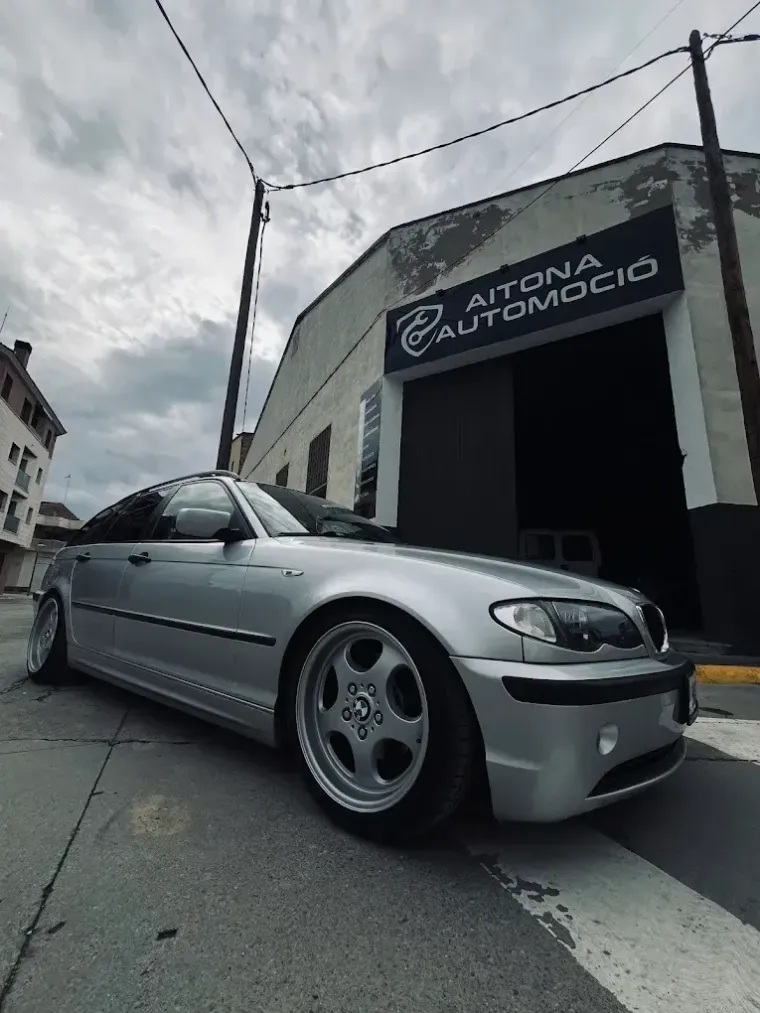 BMW sedán plateado aparcado delante de un garaje, AITONA AUTOMOCIO, en un día nublado.
