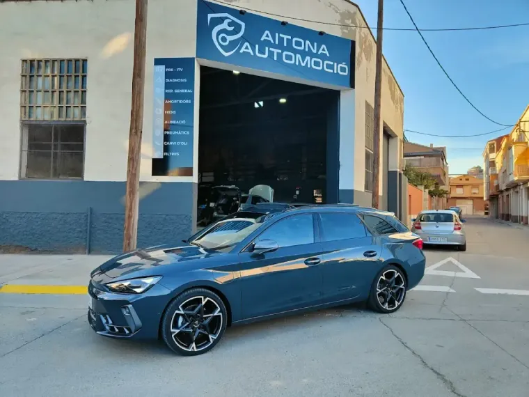 Coche azul aparcado delante de un taller mecánico llamado AITONA AUTOMOCIO; día soleado.