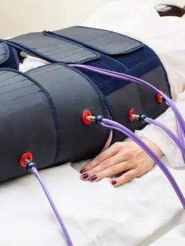 Una persona acostada con un dispositivo de terapia de compresión en los muslos y el abdomen; conectados por tubos de color púrpura.