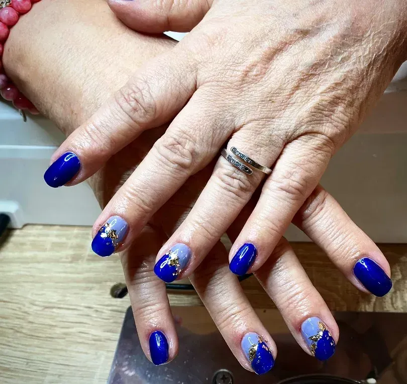 Manos con uñas decoradas en azul y gris. Algunas uñas son de un azul intenso, otras grises con detalles dorados.