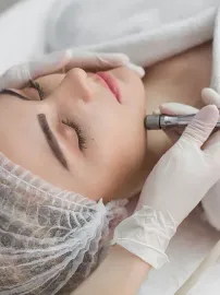Mujer recibiendo un tratamiento facial con un dispositivo, realizado con guantes. Tiene los ojos cerrados y la imagen es blanca.
