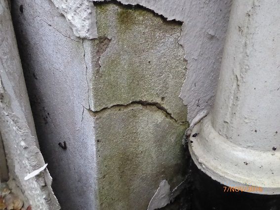 Riss, Schimmel und Algenbewuchs und abblätternder Putz an einer Außenwandecke