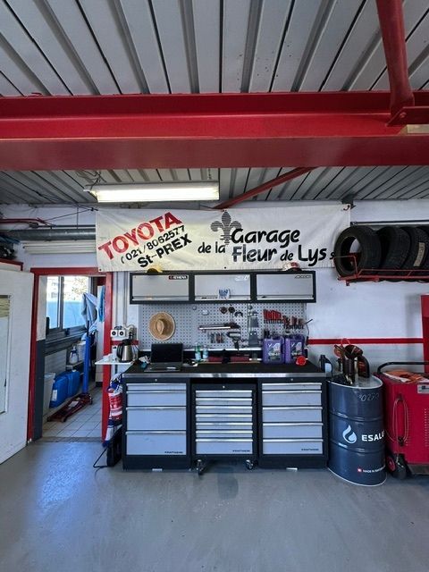 Intérieur d'un atelier automobile avec poutres de toit rouges, logo Toyota, armoires à outils et un fût bleu