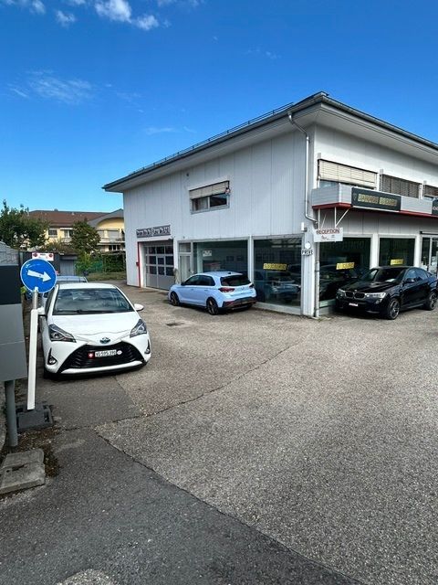Bâtiment blanc avec des voitures garées sur un parking goudronné sous un ciel bleu azur.