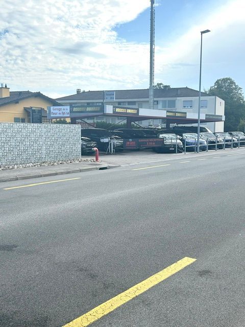 Parking devant un bâtiment bas, plusieurs voitures garées le long du trottoir sous un ciel bleu.