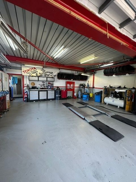 Intérieur d'un garage de réparation automobile avec poutres rouges, ponts élévateurs et équipements sur un sol en béton
