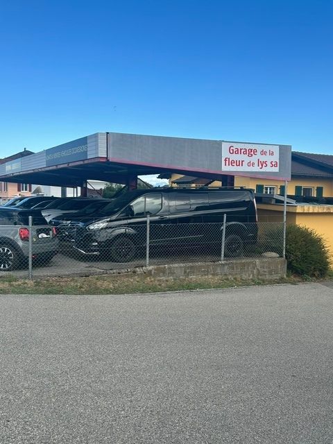 Deux voitures garées sous un abri métallique à côté d'un bâtiment, avec un panneau indiquant « Garage à louer ».