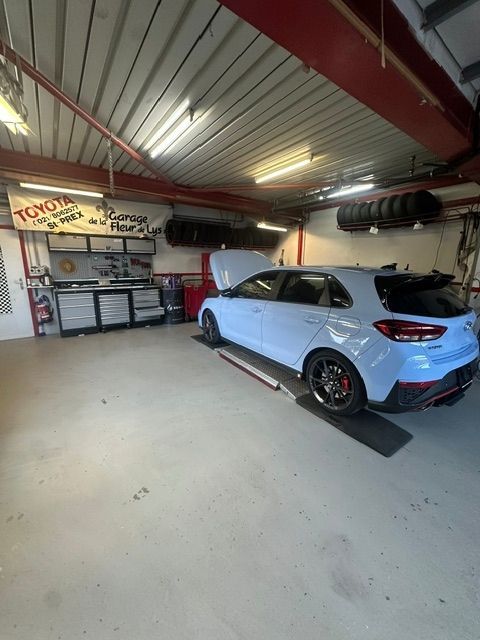 Voiture de sport bleue dans un garage, capot ouvert, garée à côté d'outils et d'équipements.