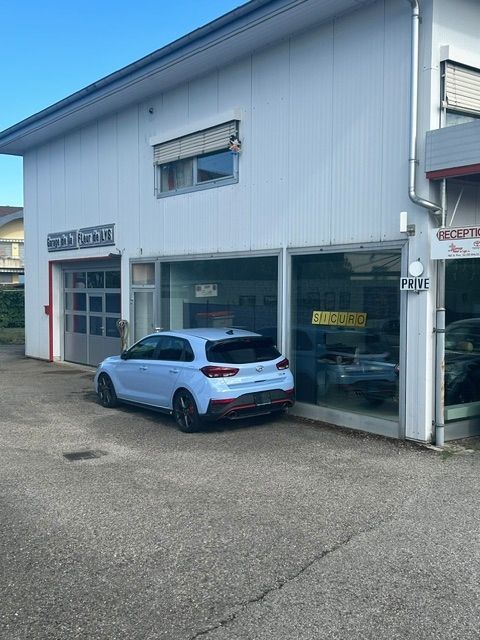 Un SUV bleu est garé devant un garage automobile à la façade vitrée, avec un extérieur et un espace de garage blancs.