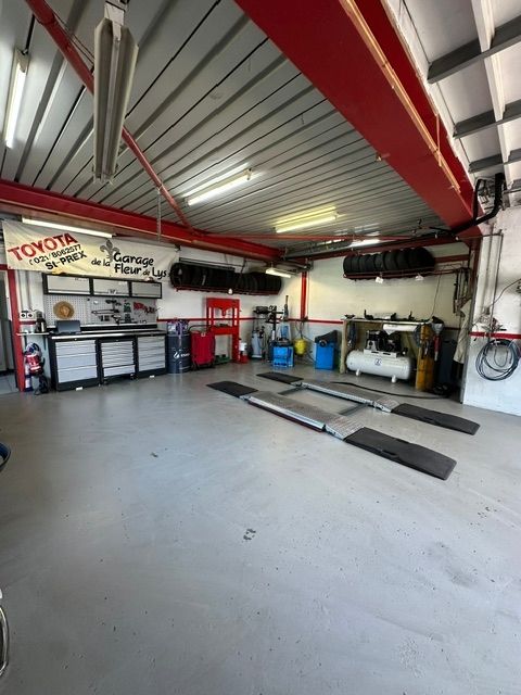 Atelier de réparation automobile vide avec poutres rouges, armoires à outils, pont élévateur et pneus sur un sol en béton