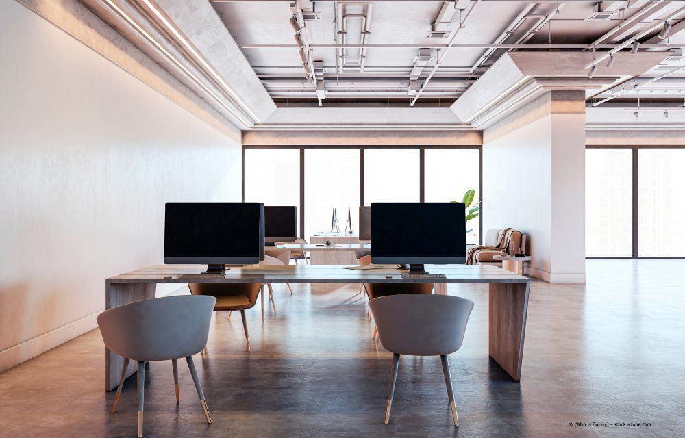 Eine Person sitzt an einem Schreibtisch, neben einem Laptop und einer kleinen Pflanze, und benutzt einen Taschenrechner und schreibt auf Papier.