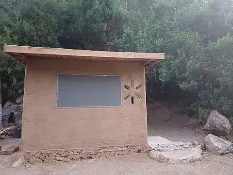 Un pequeño edificio con una pizarra al costado en el medio de un bosque.