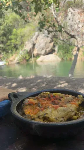 Una cacerola con comida está sobre una mesa al lado de un río.