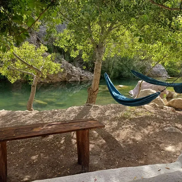 Una hamaca cuelga sobre un banco de madera al lado de un río.