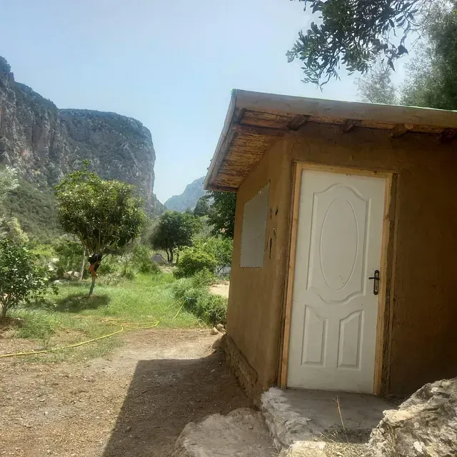 Un pequeño edificio con una puerta blanca y una montaña al fondo.
