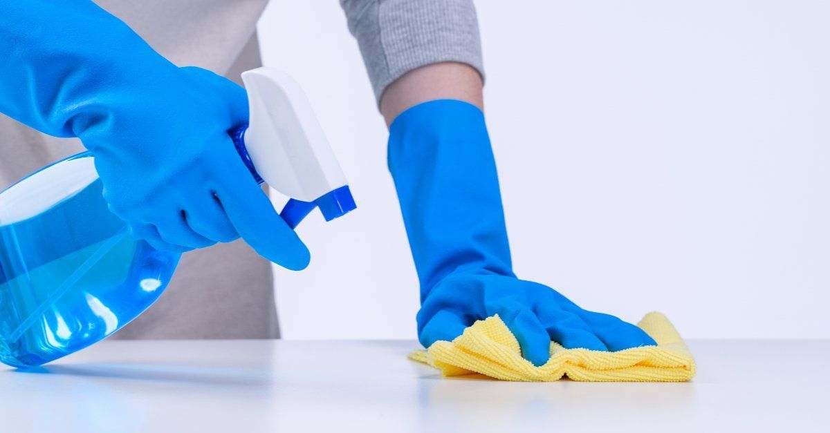 Una persona que lleva guantes azules está limpiando una mesa con un paño y una botella de spray.