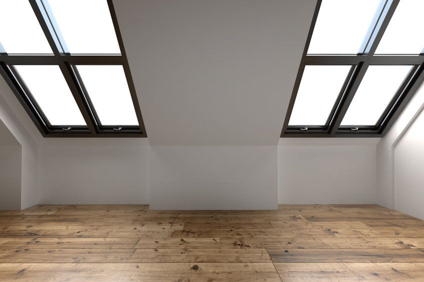 Una habitación vacía con suelo de madera y tragaluces en el techo.