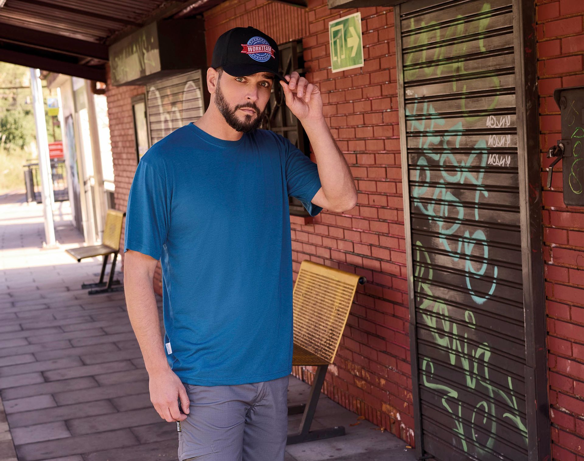 Un hombre que lleva una camisa azul y un sombrero negro está parado frente a un edificio de ladrillos.