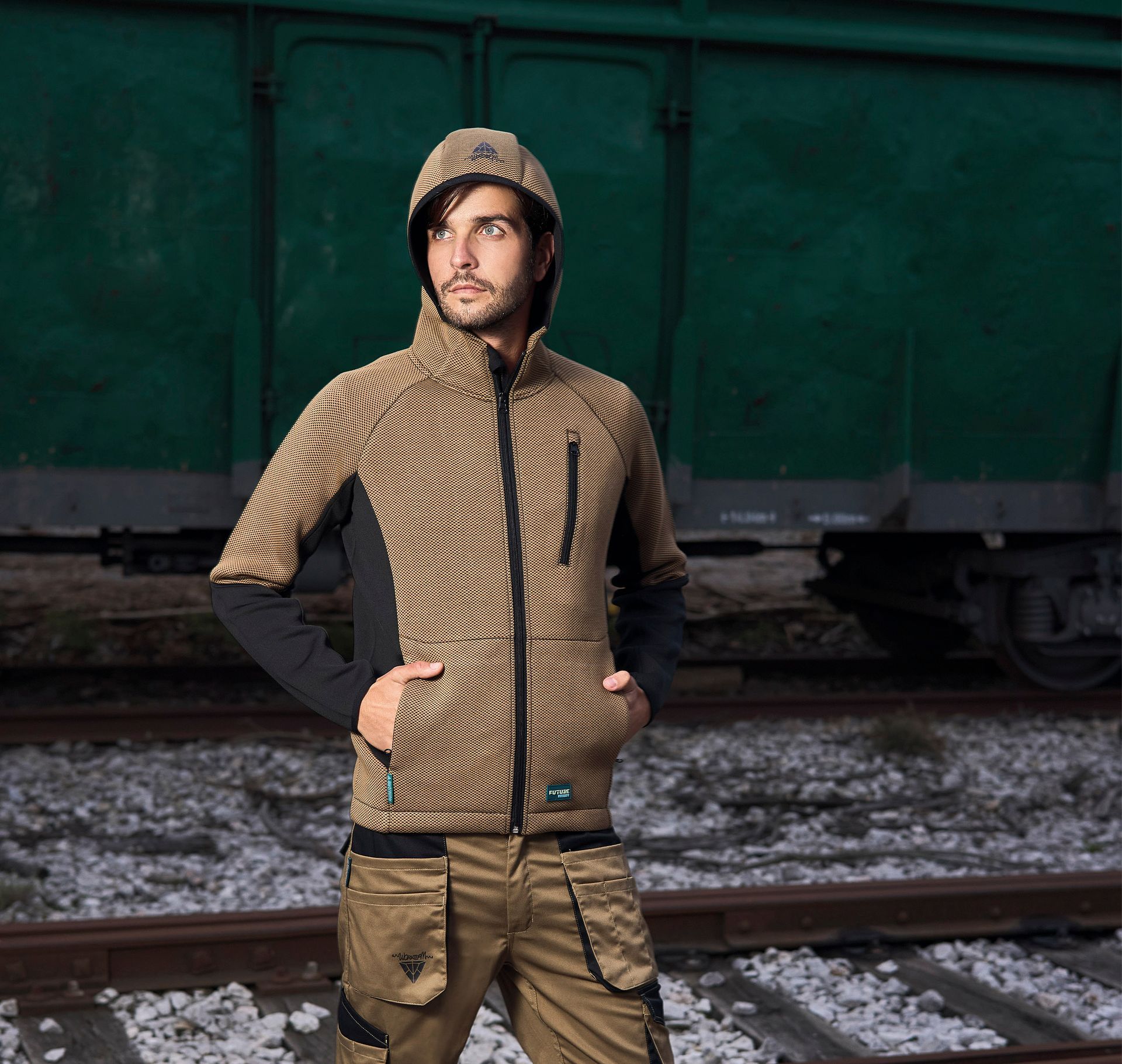 Un hombre que lleva una chaqueta con capucha está parado sobre las vías del tren.