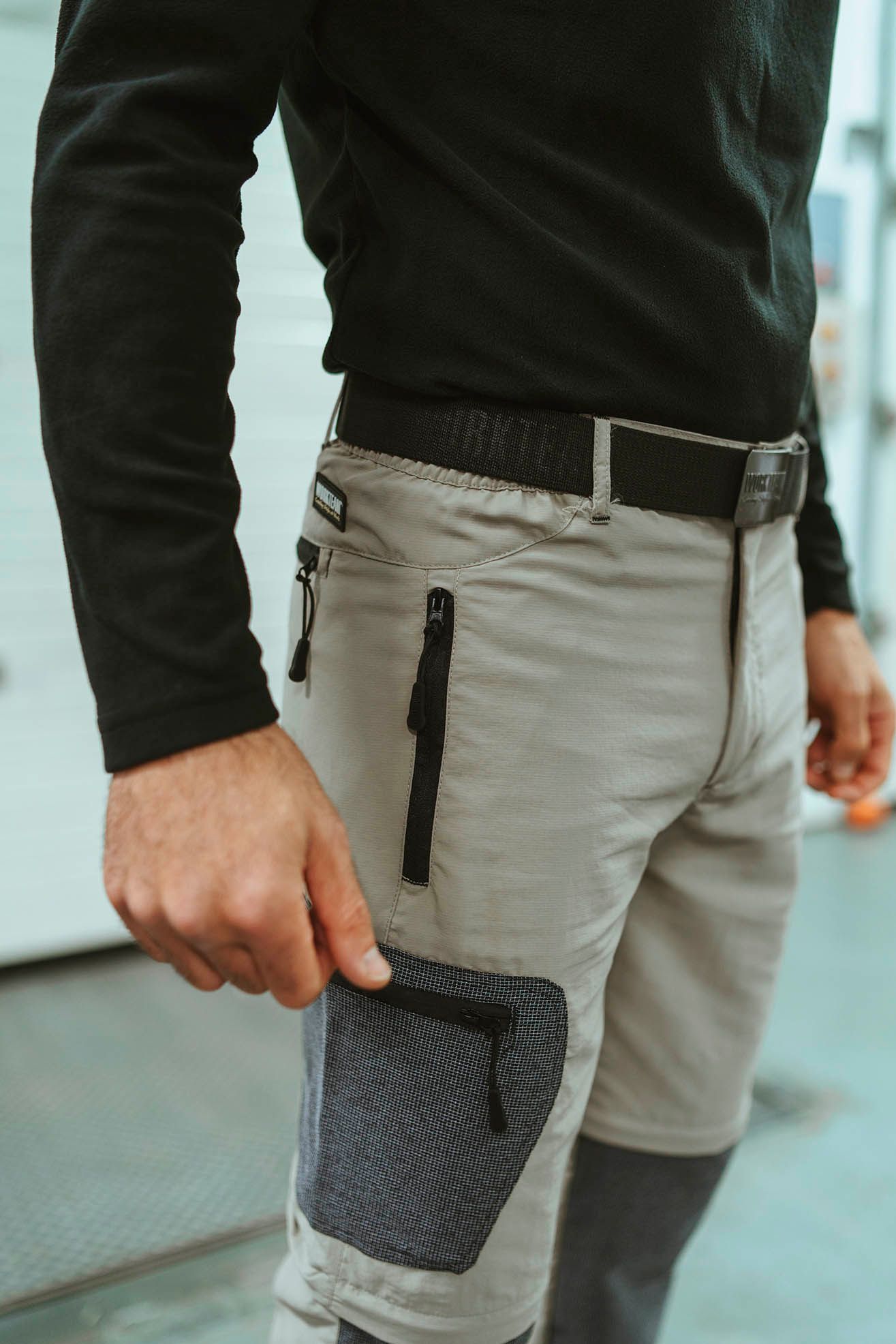 Un hombre que lleva una camisa negra y pantalones grises se guarda algo en el bolsillo.