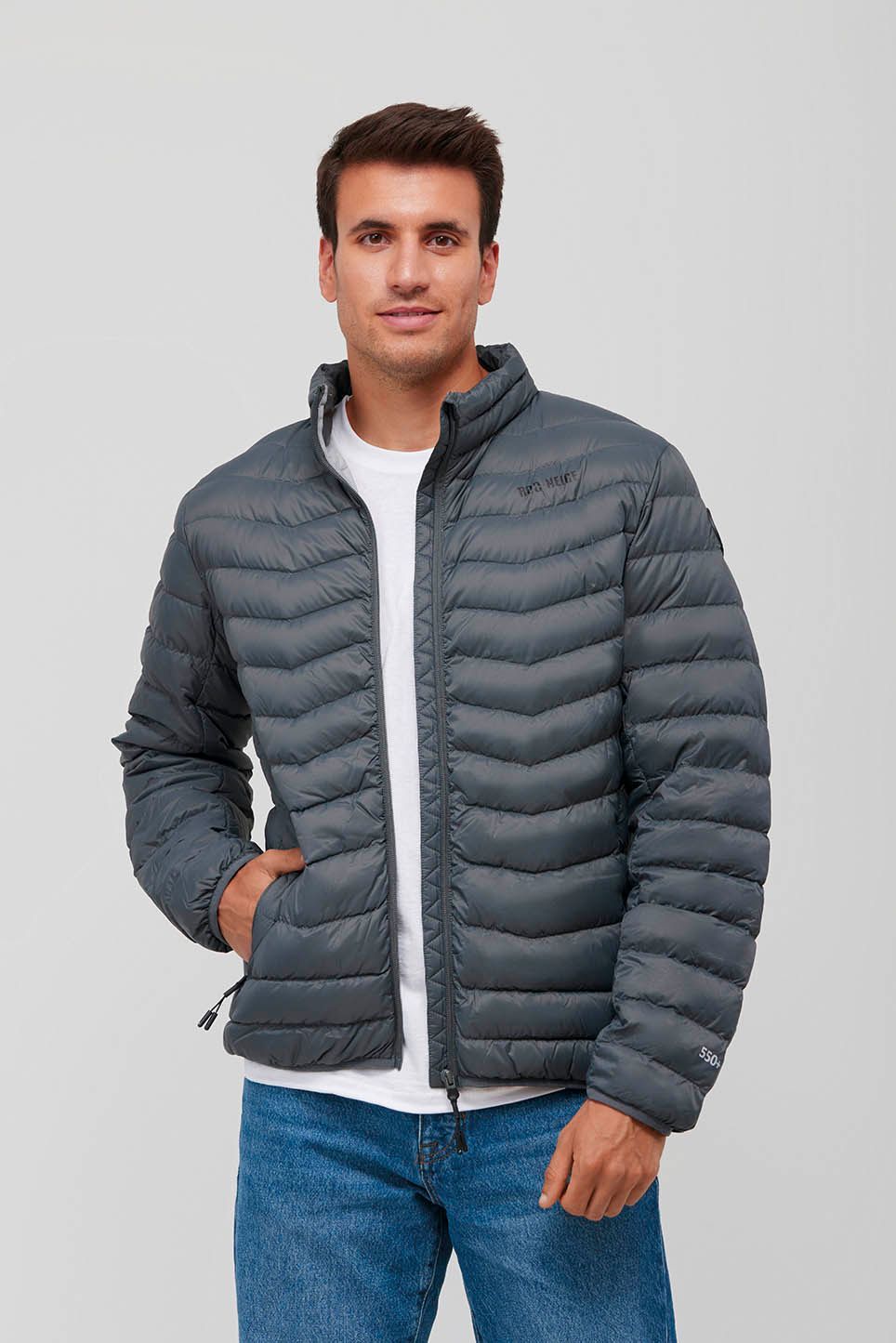 Un hombre lleva una chaqueta acolchada gris y vaqueros.