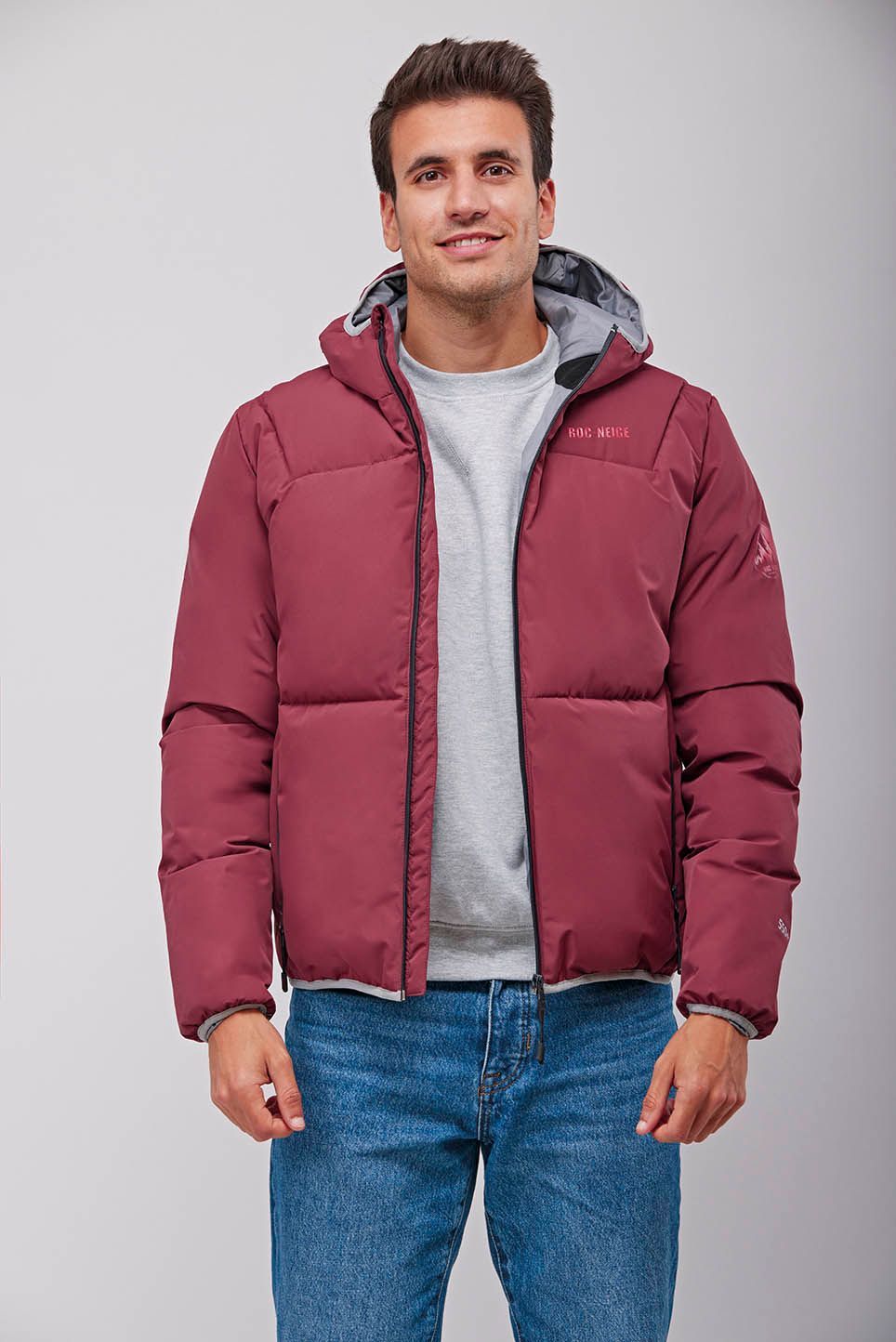 Un hombre lleva una chaqueta marrón con capucha y vaqueros.