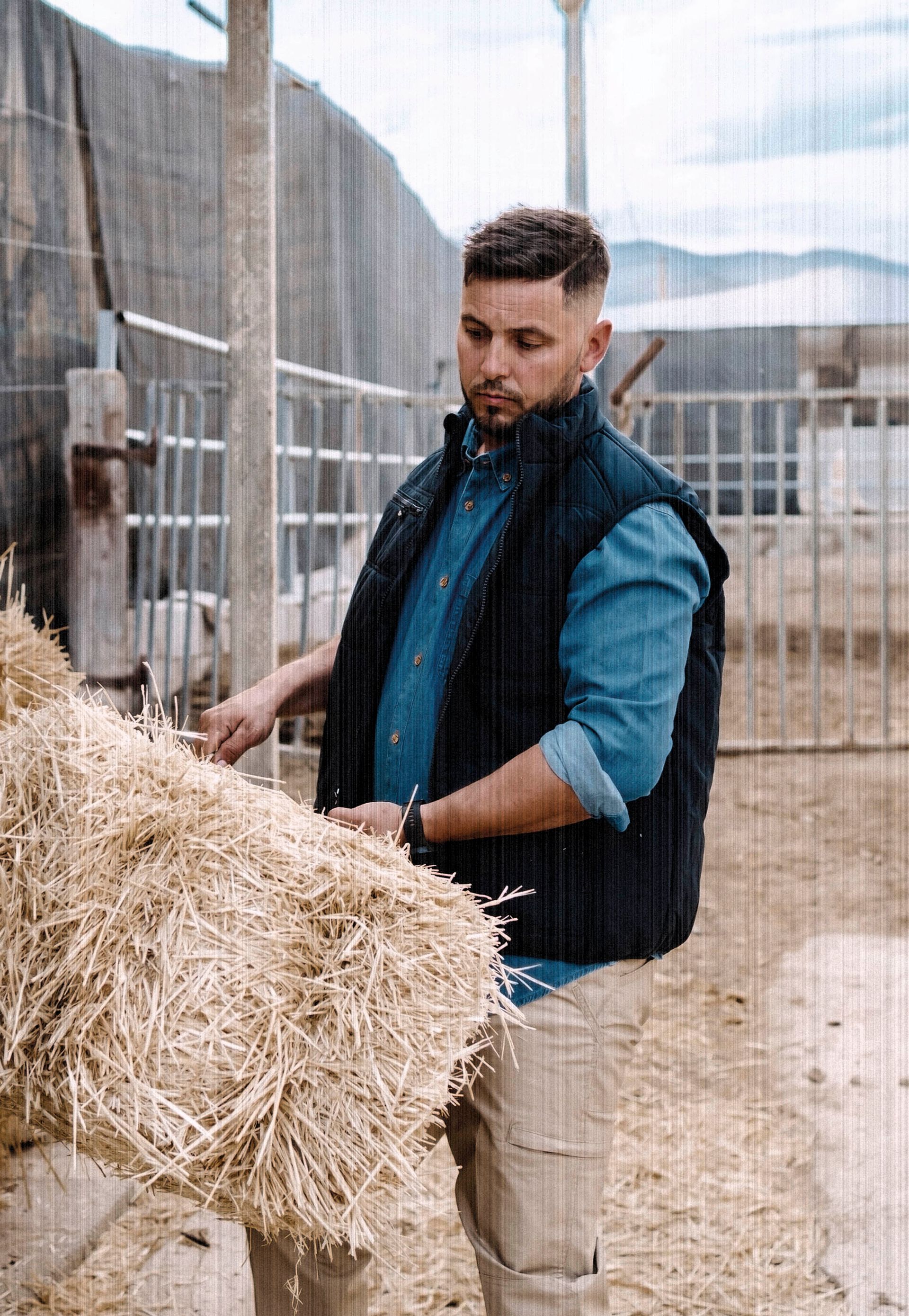 Un hombre está de pie junto a una pila de heno.