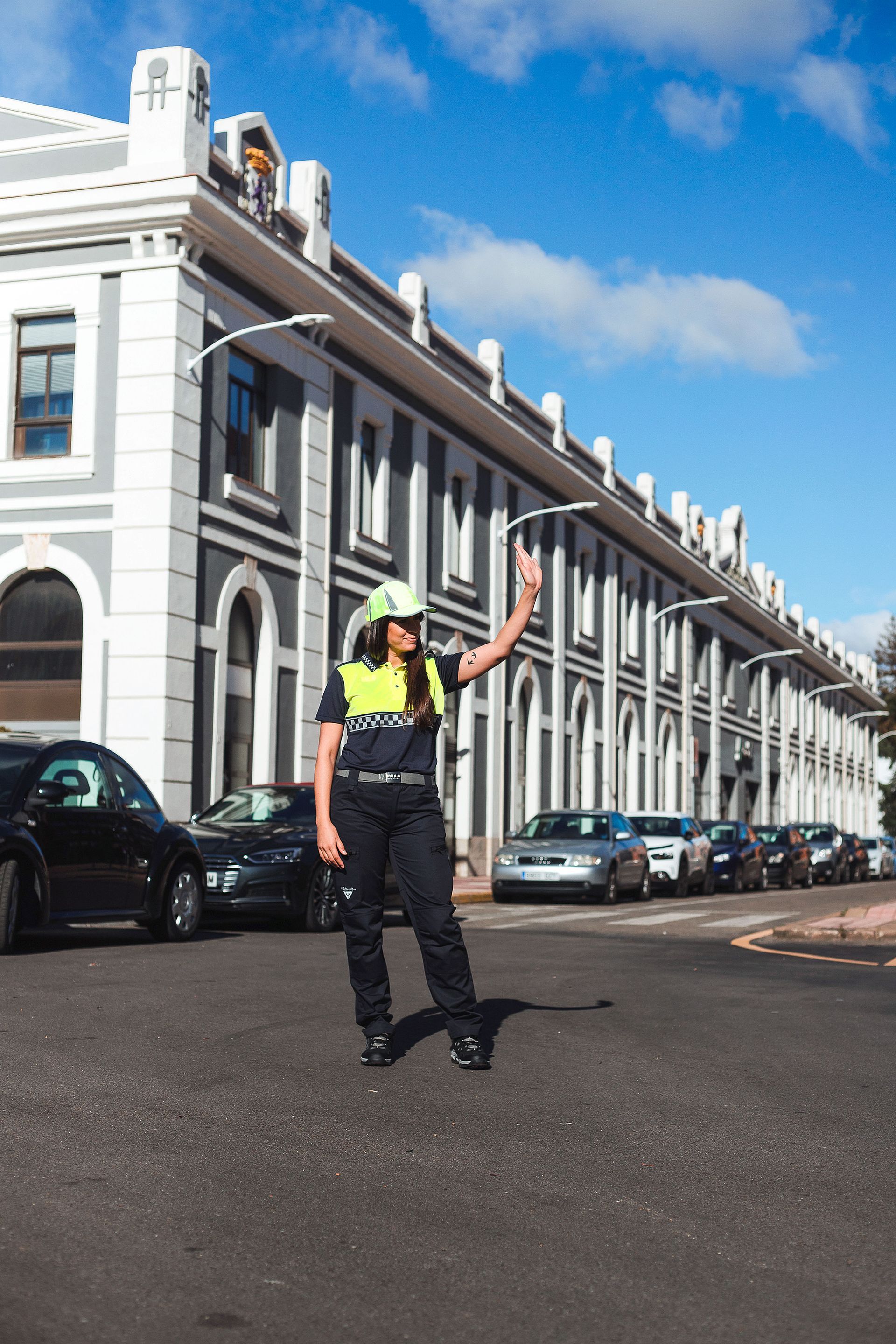 Una mujer con un chaleco amarillo está parada en una calle frente a un edificio.