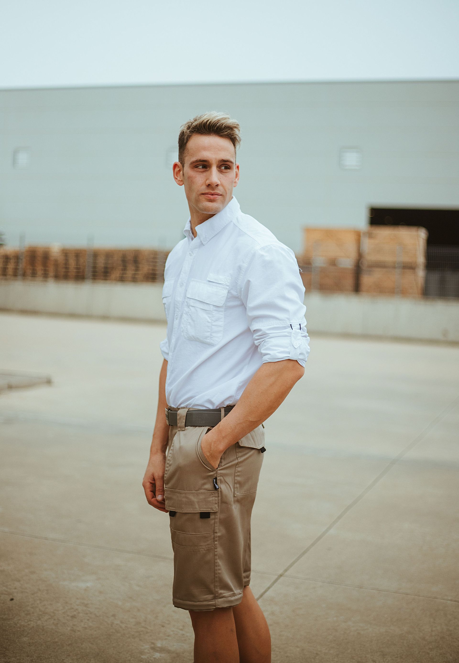 Un hombre con una camisa blanca y pantalones cortos color caqui está parado frente a un edificio.