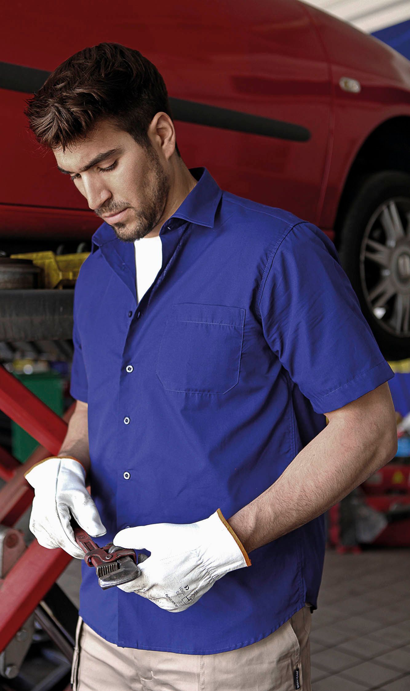 Un hombre con camisa azul y guantes blancos está trabajando en un automóvil.