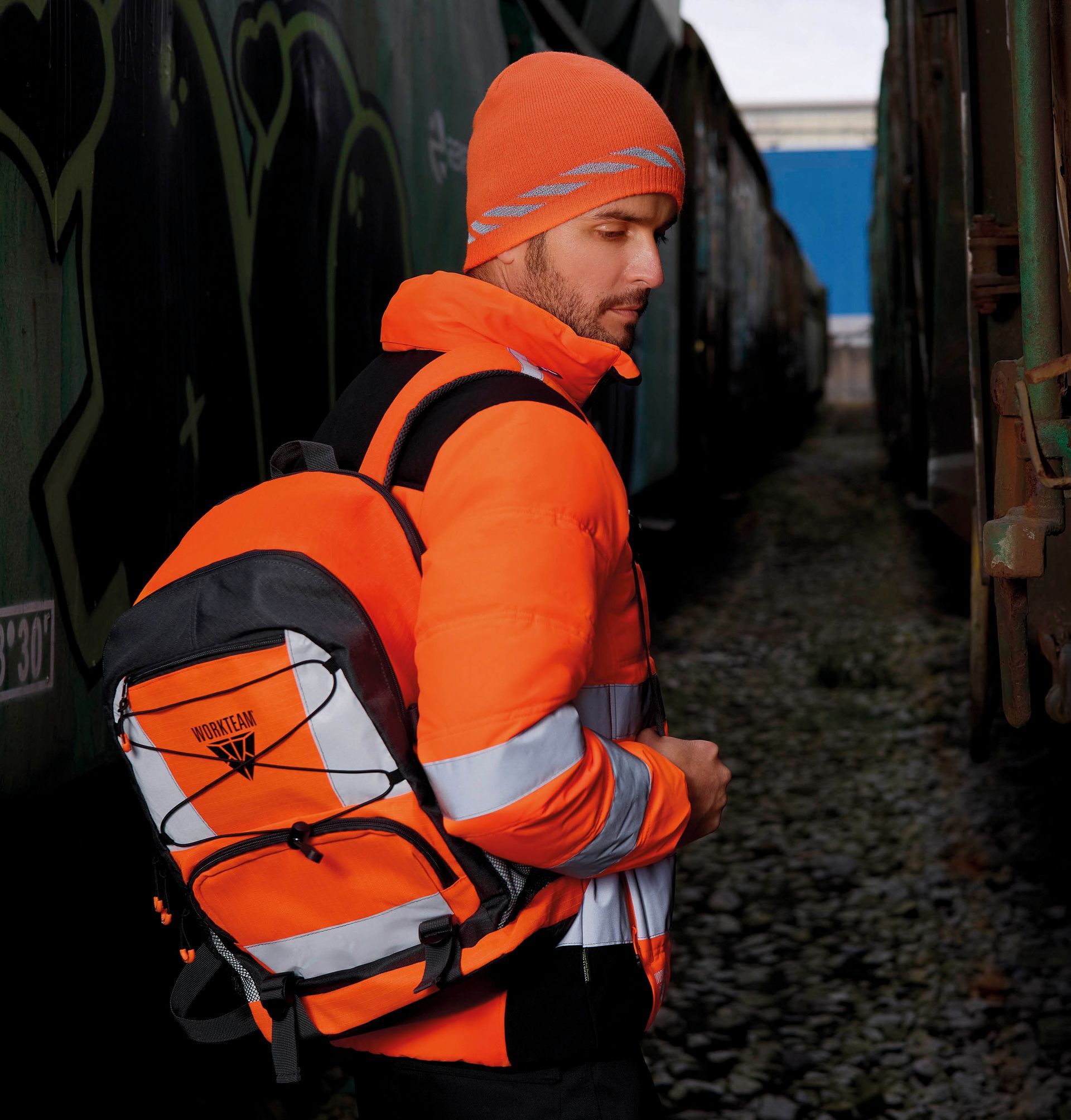 Un hombre que lleva una chaqueta y un sombrero naranja lleva una mochila adidas naranja.
