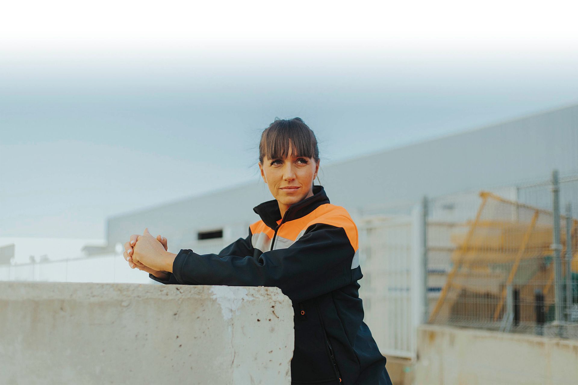 Una mujer está apoyada contra una pared de hormigón frente a un edificio.
