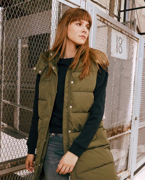 Una mujer que lleva un chaleco verde está parada frente a una valla con el número 18.