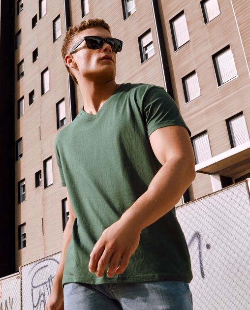 Un hombre con gafas de sol y una camisa verde camina frente a un edificio.
