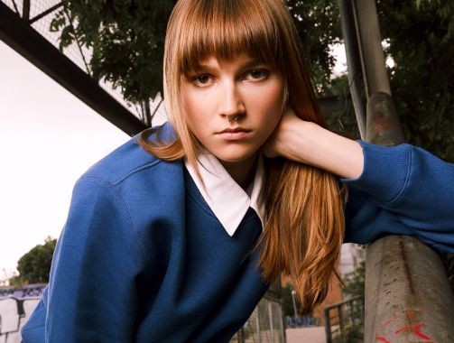 Una mujer que lleva un suéter azul y un cuello blanco está apoyada en una barandilla.