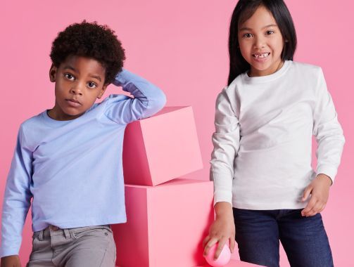 Un niño y una niña están parados uno al lado del otro sobre un fondo rosa.