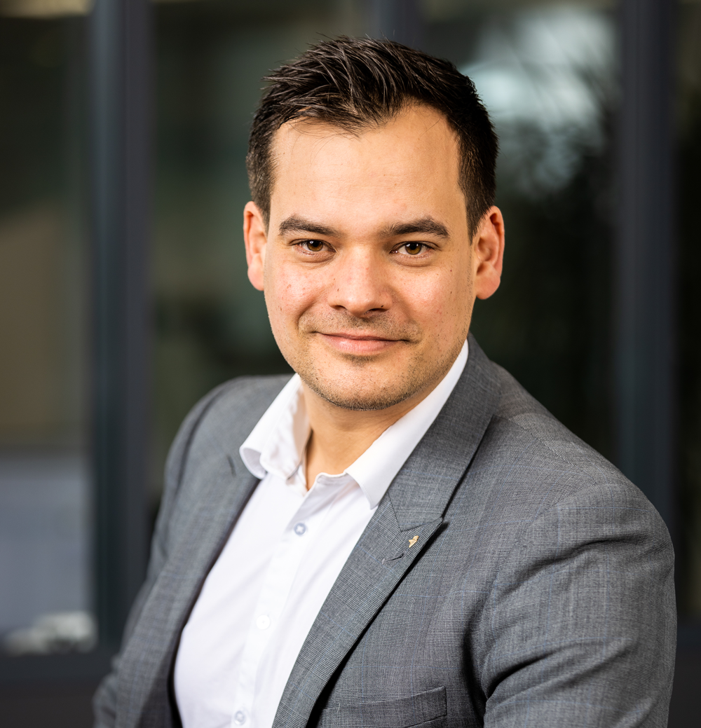 Maxime BOSNET en costume et chemise blanche sourit à la caméra.