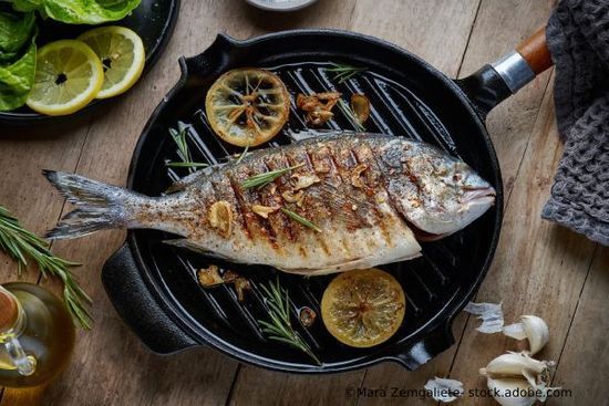 Gegrillter Fisch in einer Pfanne mit Zitronenscheiben, Rosmarin und Knoblauch auf einem Holztisch.