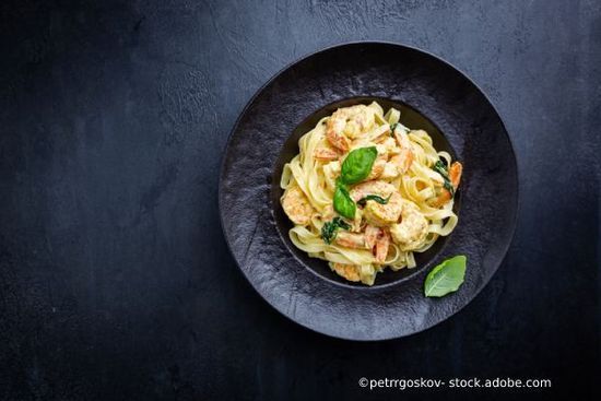 Garnelen-Fettuccine Alfredo mit Basilikum auf einem schwarzen Teller, angerichtet auf einer dunklen Oberfläche.