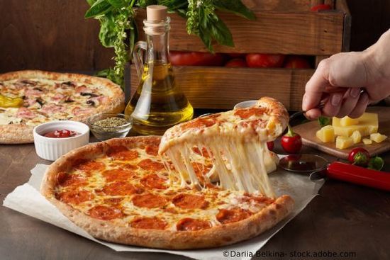 Stück Peperoni-Pizza mit Käseaufstrich; eine Person hebt ein Stück hoch; Zutaten auf einem Holztisch.