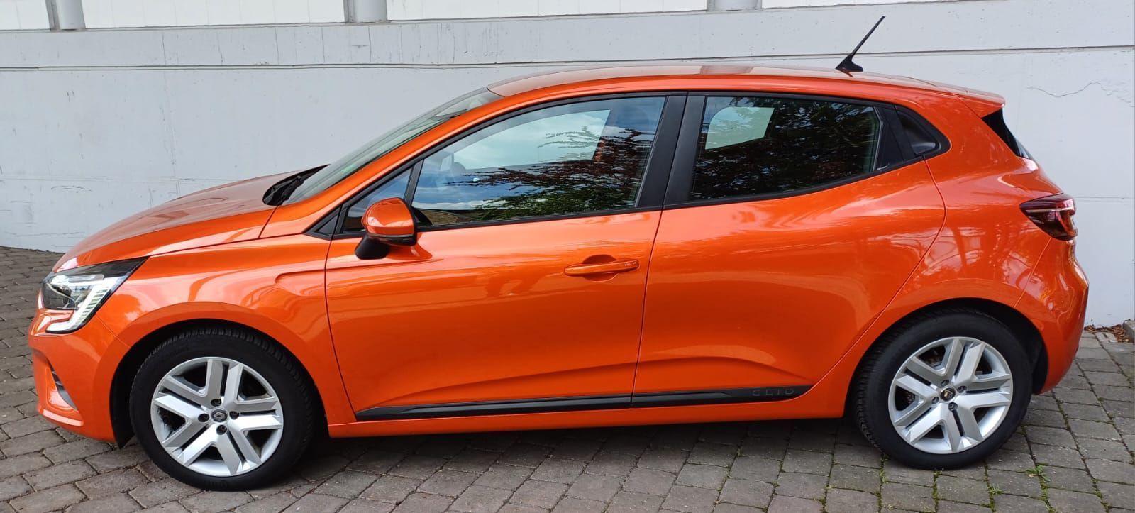 Fahrzeugmodelle Oranger Kompaktwagen mit Schrägheck, geparkt auf einer gepflasterten Straße, Seitenansicht