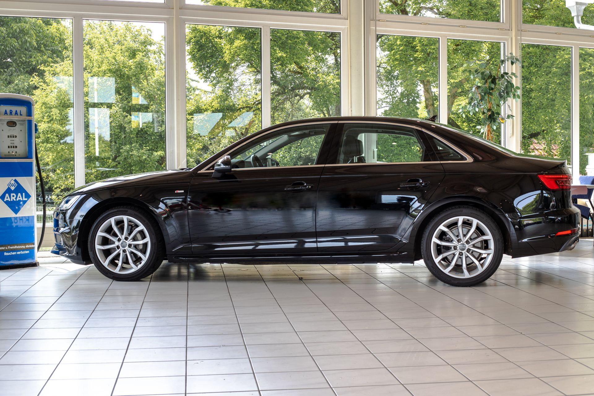 Fahrzeugmodelle Eine schwarze Limousine parkte in einem hellen Ausstellungsraum mit großen Fenstern und Fliesenboden