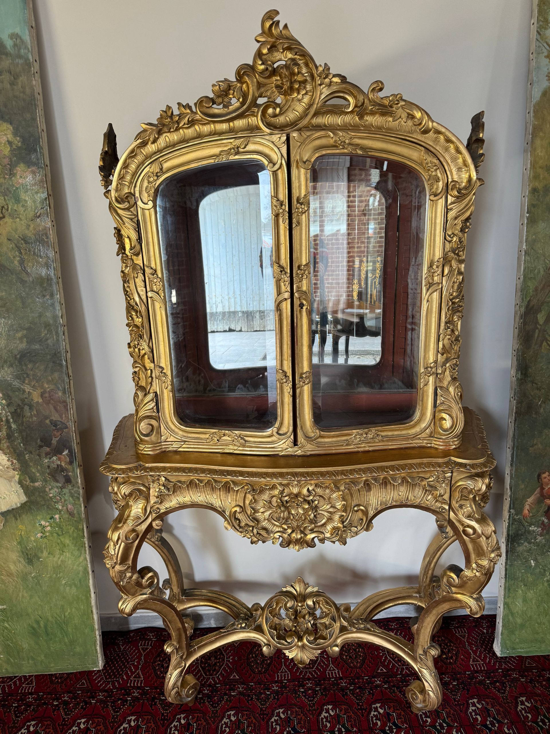 Importante et rare  vitrine en bois doré d'époque Napoléon III de style Louis XV.,
De forme galbée reposant sur une console (meuble en deux parties).
L'ensemble de ce meuble en bois doré  est richement sculpté de feuillage, guirlande de fleurs, coquilles,
La vitrine est vitrée en verre biseauté en facade et sur les côtés, ouvre à une porte et deux étagères,  elle est surmontée d'une rosace, 
la console  repose sur  quatre pieds  dits escargots, lesquels sont  reliés par une entretoise avec un rosace de ffleurs dans son centre et une rosace de fleurs en ceinture et possède un tiroir.
Inscription au dos de ce meuble le nom du doreur. Photo jointe.
Belle dorure à la feuille d'or.