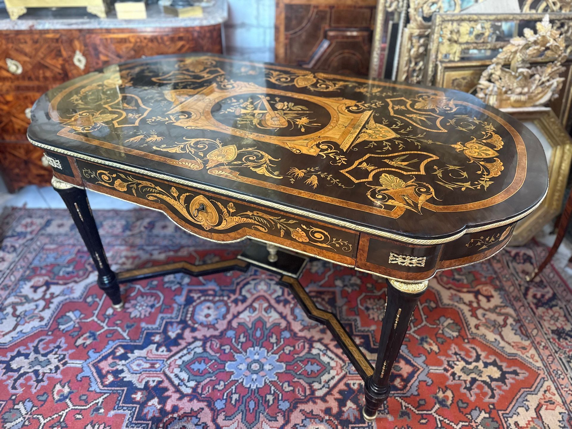 Belle table de milieu d'époque Napoléon III – Style Louis XVI, richement marquetée de différents bois indigènes sur bois noirci . (Citronnier, loupe de noyer, noyer, bois teinté vert, 
Le plateau présente un décor varié soit instruments de musique, oiseaux, papillons, feuillages, feuilles d’’acanthe, pourtour d’une frise en laiton 
Elle ouvre par un grand tiroir central à décor de marqueterie,
Et repose sur des pieds fuselés cannelés avec bague en bronze, reliés par une entretoise mouvementée surmontée d’une cassolette en bronze doré dans son milieu, 
La cassolette présentant un décor de tête de bélier de chaque côté et flambeau,
Vernis au tampon à l’ancienne.
A propos de Charles-Guillaume Diehl, né le 28 juillet 1811 à Steinbach (länder de Hesse en Allemagne) et mort le 20 juin 1885 à Chessy (Seine-et-Marne), est un ébéniste, spécialisé dans la création de petits meubles. Il est naturalisé français en 1872.
Il s'établit à Paris en 1840. Il est répertorié en 1850 comme fabricant de tables.