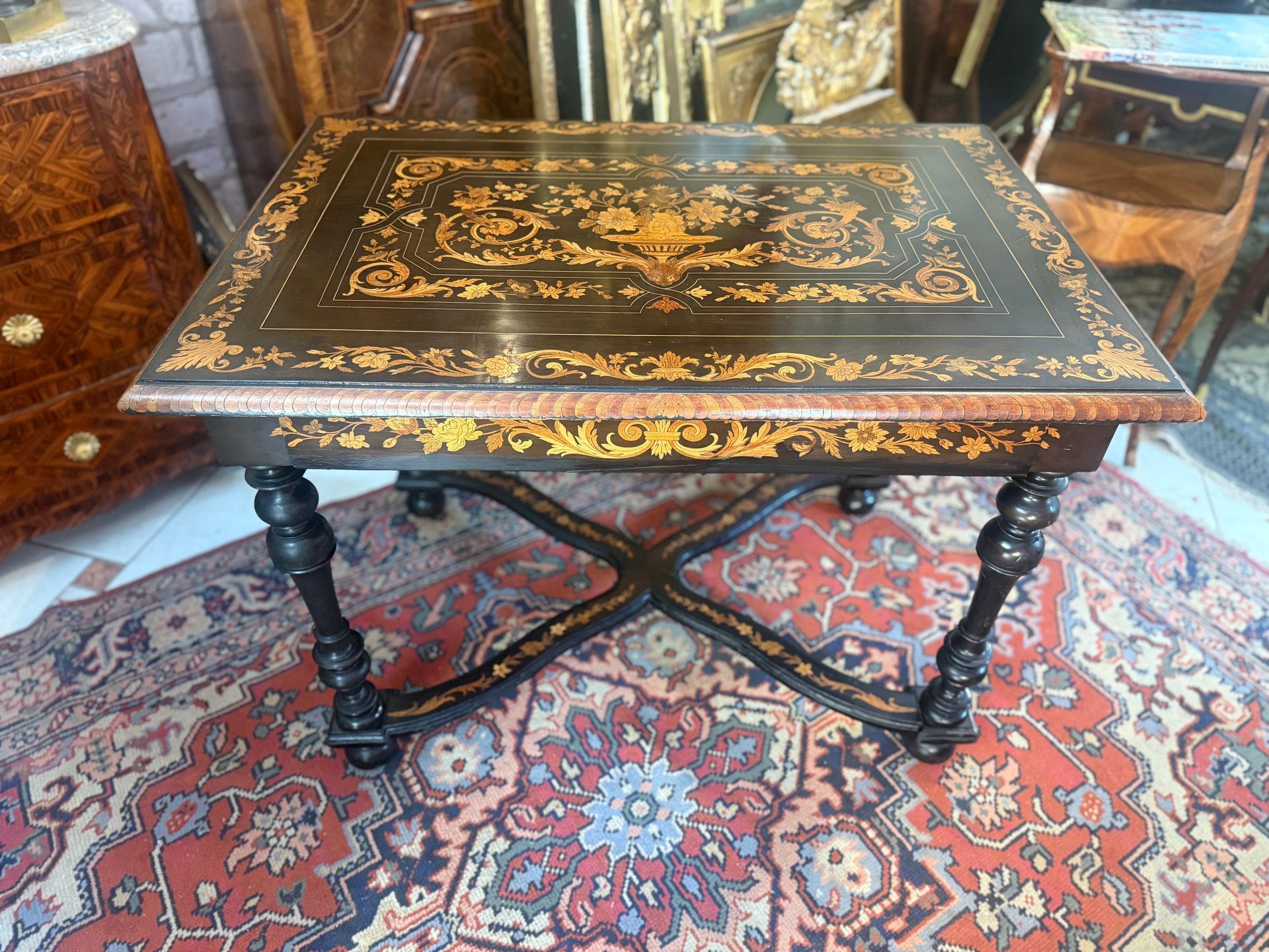 Table de milieu LOUIS XIV de style hollandaise, en marqueterie de jasmin. Le plateau présente un riche décor varié soit urne de fleurs dans son milieu, fleurs,  feuillages, feuilles d'acanthe, Elle ouvre par un  grand tiroir en ceinture avec décor de marqueterie Et repose sur des pieds colonnes formant des boules reliées par une entretoise à décor de marqueterie de forme  mouvementée en x.  Cette table peut servir de bureau, de salon.