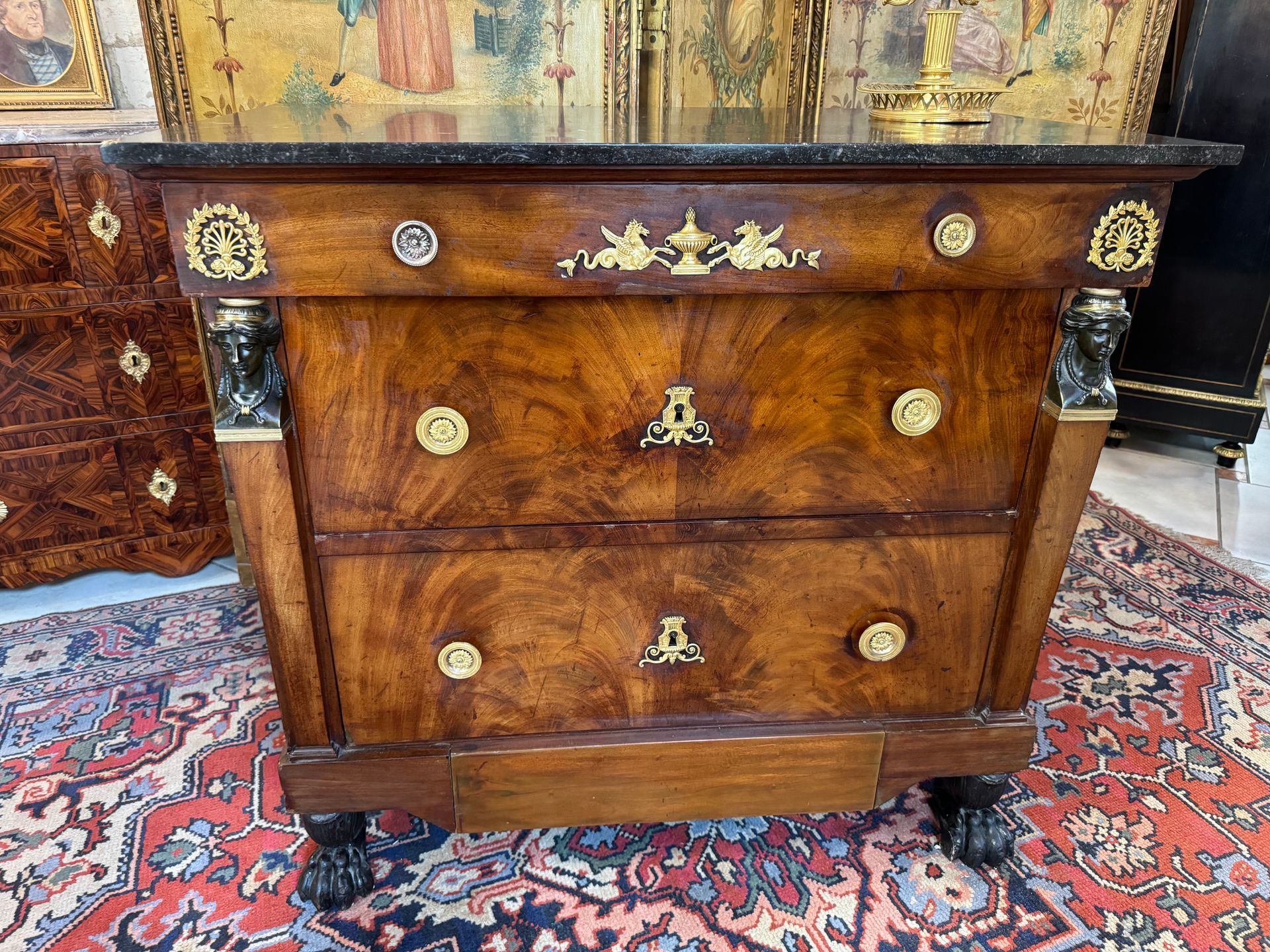 Jolie commode dite « retour d’Egypte » en acajou.
Belle garniture de bronzes dorés,
Têtes de cariatide de chaque côté, palmettes, animaux ailés,
Entrées de serrures ornées, poignées en anneaux,
Cette commode ouvre par quatre tiroirs, soit un tiroir en ceinture séparé par deux traverses, deux grands tiroirs et un petit tiroir dans la base en bas.
Elle repose sur des pieds antérieurs en griffes en bois noirci et postérieurs en chapelet.
Le tout coiffé d'un marbre noir d’origine.